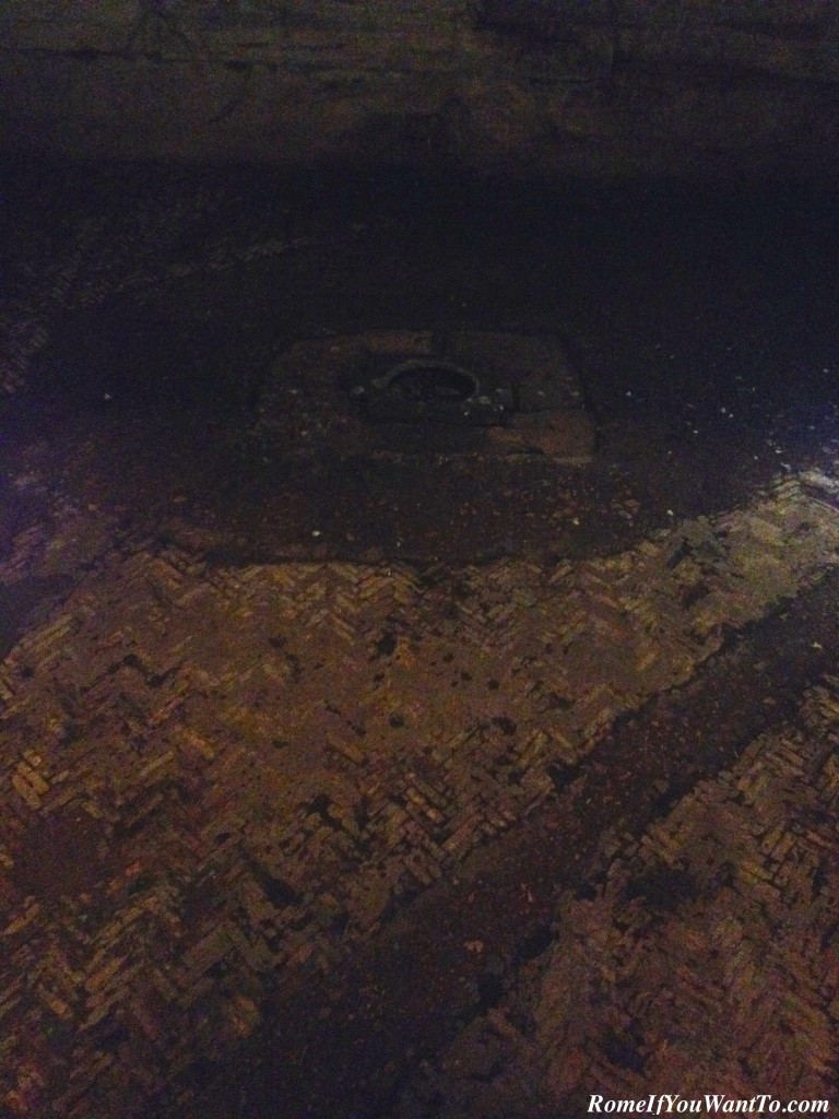 The floor of the tunnels. The bricks are original, 2000 years old. The circle in the square would have anchored a thick iron chain. The chain would have been part of a mechanism to pull open or closed trap doors in the floor above, through which animals and people would enter to the sounds of cheers and jeers.